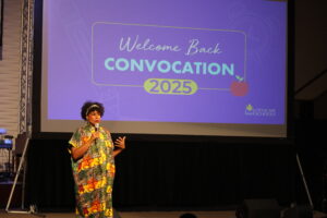 A person speaks on stage in front of a large screen displaying "Welcome Back Convocation 2025" and the Cityscape Schools logo, celebrating the start of a new academic year at Cityscape Schools.