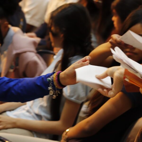 Students seated in an auditorium pass paper ballots hand to hand during East Grand Preparatory student council election.